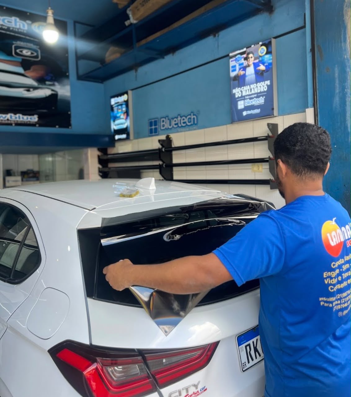 Profissional da Lanna’s Sound aplicando película no vidro traseiro de um carro branco